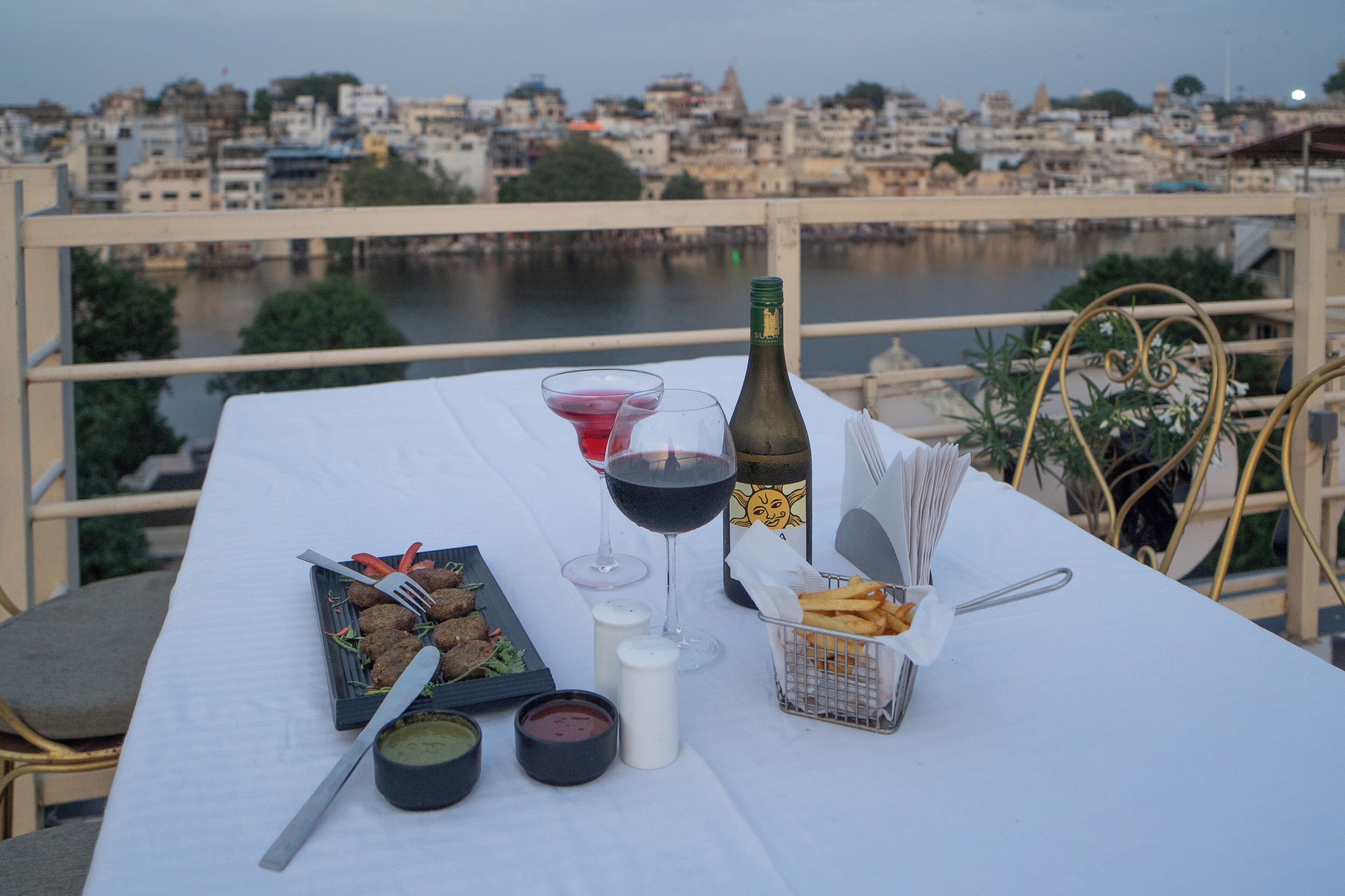 Une table dressée avec de la nourriture, des boissons et des condiments, offrant une vue sur le paysage urbain et la rivière.