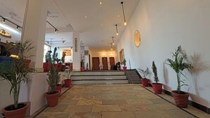 Hall dell'hotel con pavimento in pietra, piante in vaso, una scala e una reception.