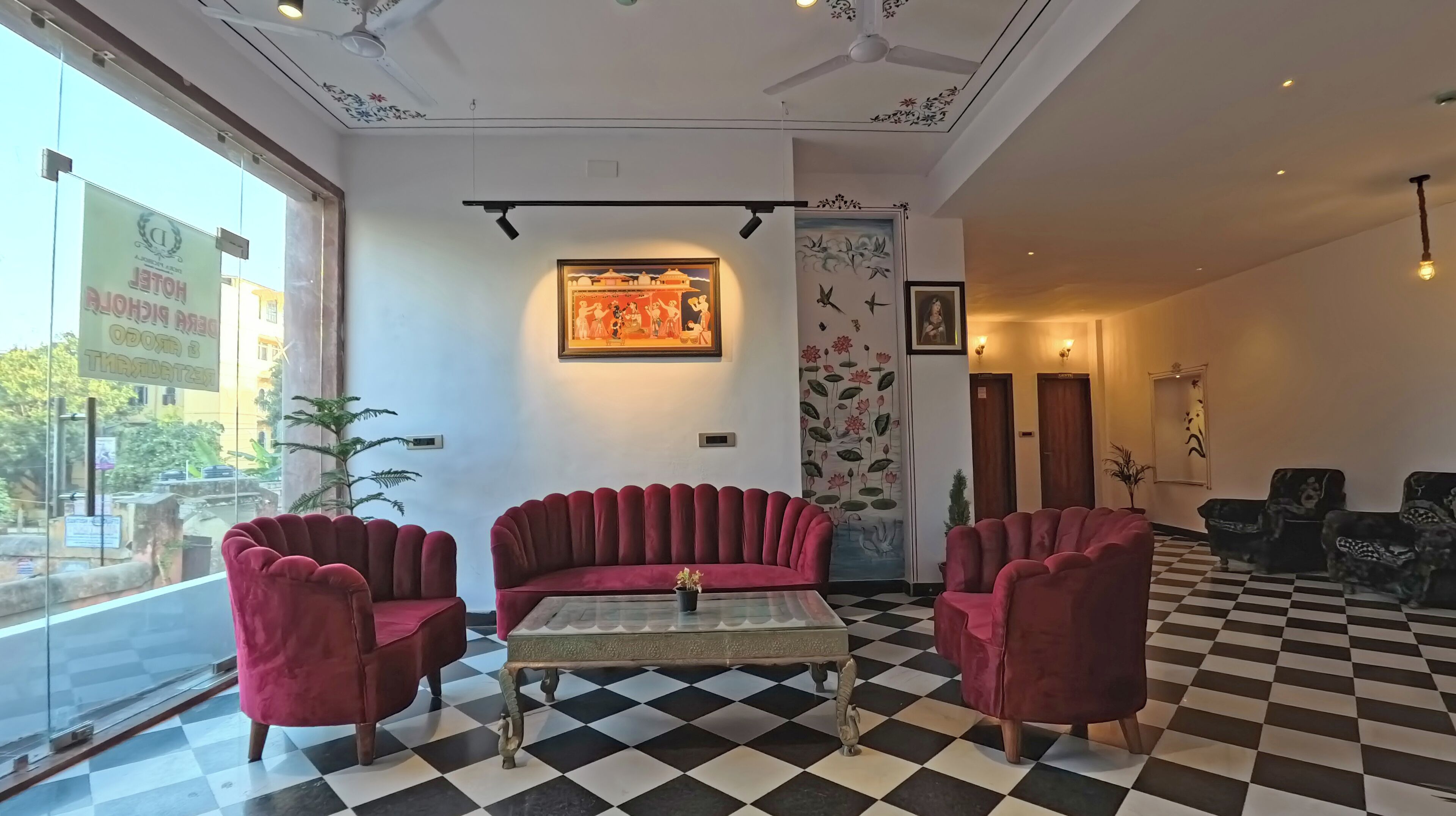 A hotel lobby with a checkered floor, red velvet sofas, and a framed painting on the wall.
