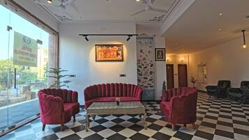 A hotel lobby with a checkered floor, red velvet sofas, and a framed painting on the wall.