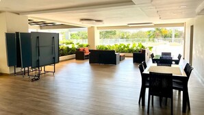 Amplio espacio interior con una mesa larga y sillas, un sofá y una pantalla grande sobre un soporte.