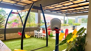 Zona de juegos al aire libre con césped artificial, columpios y una estructura para escalar.