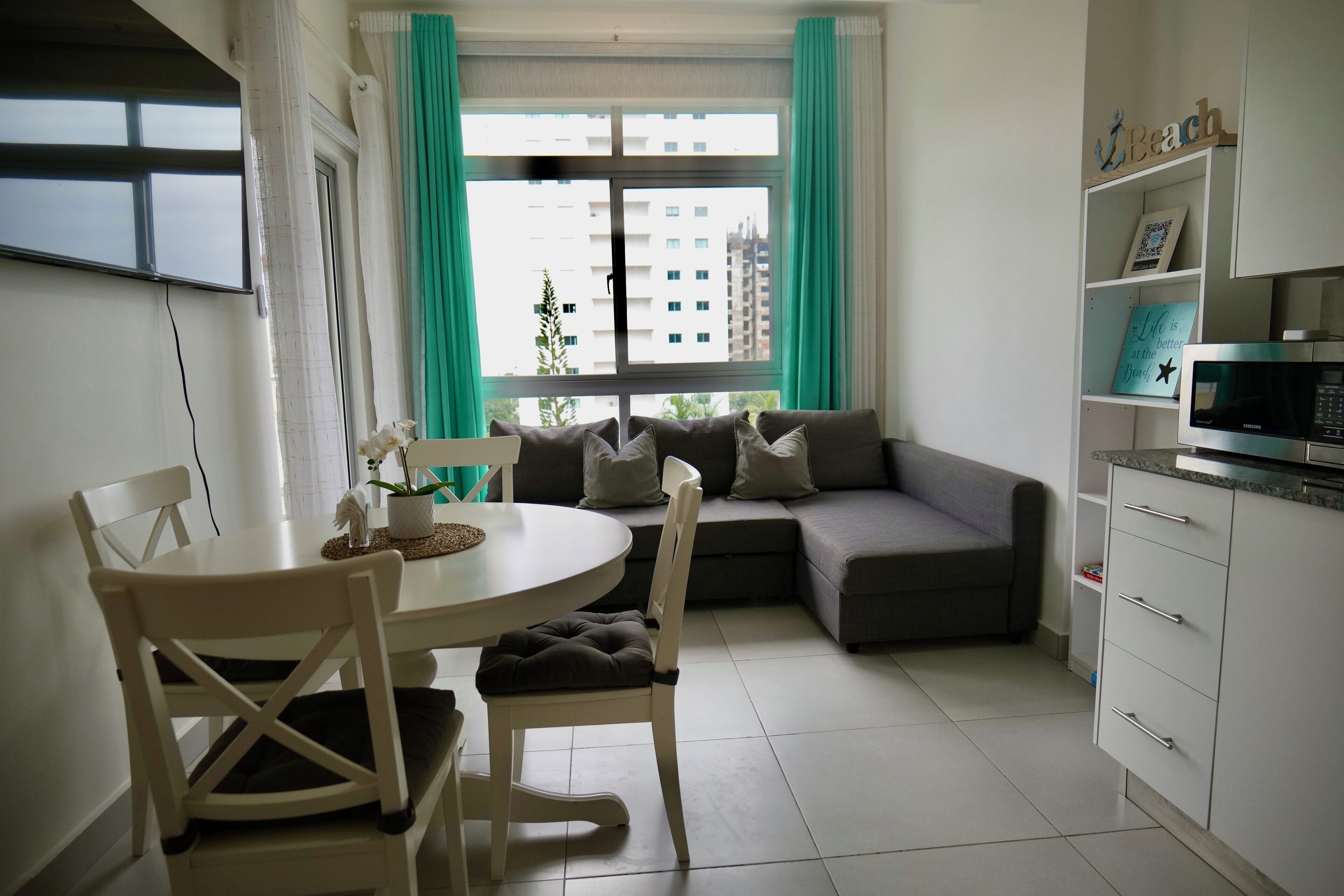 Un salon moderne comprenant un coin repas, un canapé gris et un meuble blanc contenant un four à micro-ondes.
