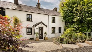 A white building with a black door and windows, surrounded by gravel and plants. - The Coronation Family Cottage | Ridgestone (Lindale)