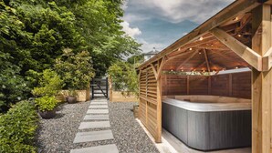 A wooden hot tub area with a stone pathway leading to a gate. - The Coronation Family Cottage | Ridgestone (Lindale)