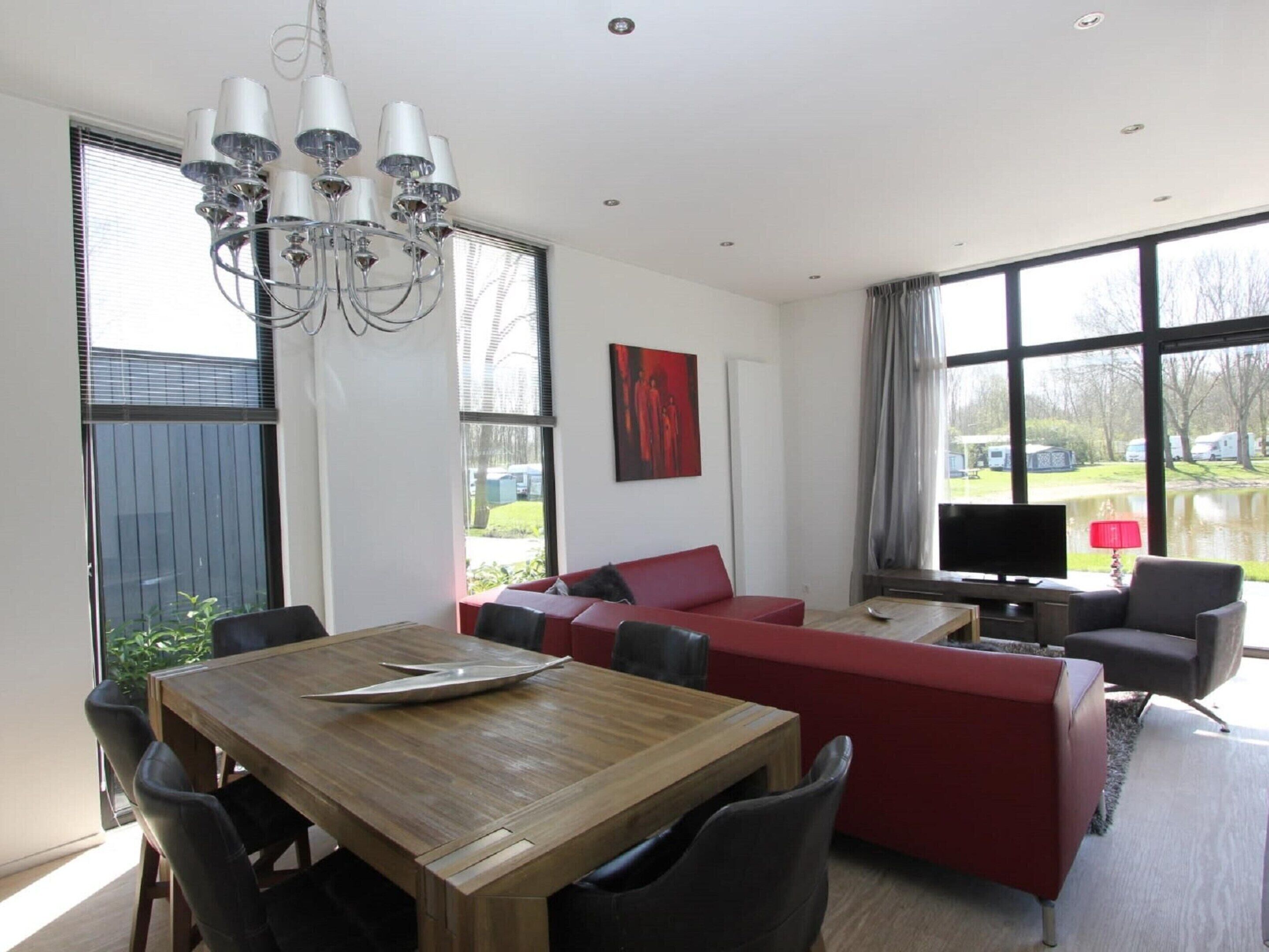 A modern living room with a wooden dining table, red sofa, and a TV.