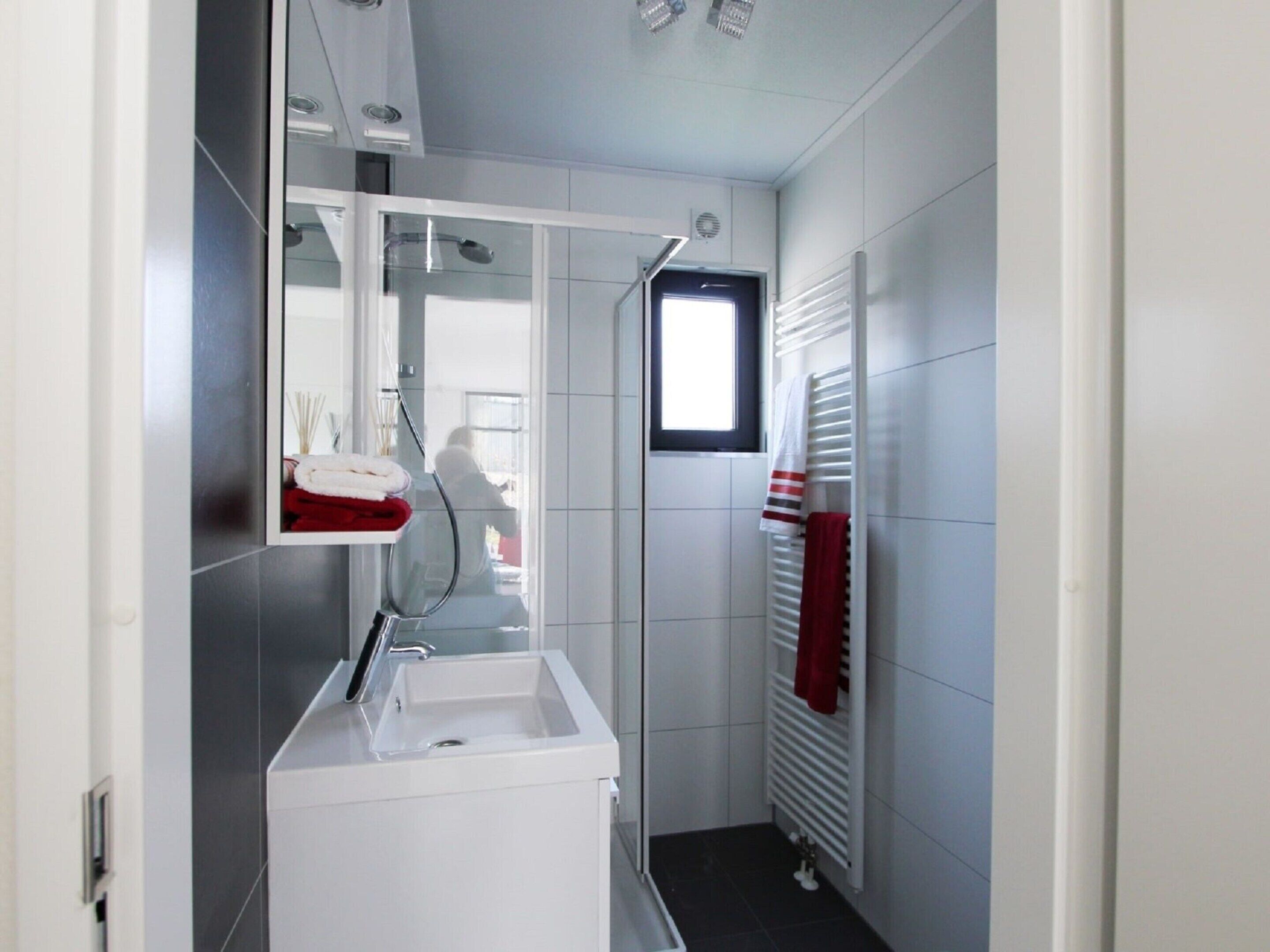 A modern bathroom with a white sink, mirror, and towel rack.