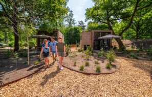 A garden area with wooden structures, possibly for dining or relaxation, surrounded by trees and plants. - Modern Holiday Home in a Holiday Park (Arnhem)
