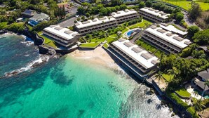 Ein Küstenresort mit mehreren Gebäuden, einem Strand und klarem türkisblauem Wasser.