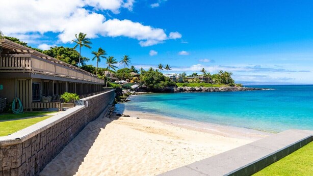 Ein Hotel direkt am Strand mit einer Steinmauer, feinem Sand und einem tiefblauen Meer.