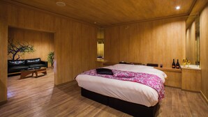 A modern bedroom with a wooden ceiling and walls, a large bed with a pink and white bedspread, a black leather sofa, and a small table with two bottles and a glass. - HOTEL elLle - Adults Only (Toyama)