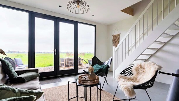 A modern living room with a sofa, a chair, a small table, and a large sliding glass door leading to an outdoor area. - Luxury Farmstay – Sleep in Style Among the Cows (Loenen aan de Vecht)
