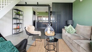 A modern living room with a sofa, a chair, a small table, and a bookshelf. There is a staircase leading to another room. - Luxury Farmstay – Sleep in Style Among the Cows (Loenen aan de Vecht)