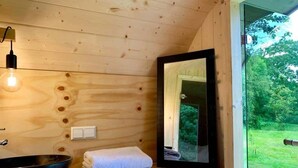 Ein Badezimmer einer Holzhütte mit einem großen Fenster, einem hölzernen Waschbecken, einem Handtuch und einer Leuchte.
