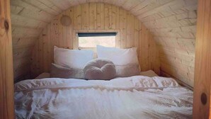 Ein gemütliches Schlafzimmer unter dem Dach mit Holzwänden, einem großen Bett mit weißer Bettwäsche und einem kleinen Fenster am Ende des Raumes.