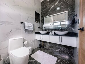 Ein modernes Badezimmer mit Toilette, Bidet, zwei Waschbecken, einem großen Spiegel und Marmorböden.