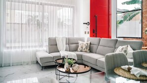A modern living room with a grey sofa, a glass coffee table, and a red door.