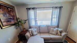 Un salon avec un canapé d’angle beige, un pouf assorti, une plante en pot et une œuvre d’art encadrée accrochée au mur.