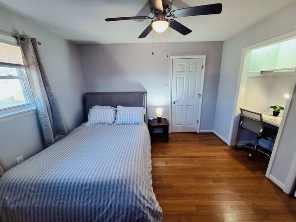 A bedroom with a bed, a nightstand with a lamp, a ceiling fan, a door, and a small desk with a chair. - Cozy 2-bedroom apartment with WiFi, AC, walk to UK Campus/Hospital, near St. Joe (Lexington)