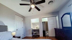 Une chambre à coucher comprenant un lit, un ventilateur de plafond, une commode et un dressing.