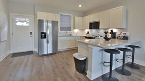 Una cocina moderna con armarios blancos, un refrigerador de acero inoxidable, un microondas y una isla de granito con taburetes de bar.