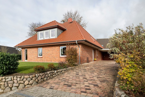 A two-story brick house with a red-tiled roof, a stone pathway leading to the entrance, and a small garden area.