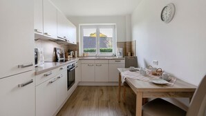 Una cocina moderna con armarios blancos, una mesa de comedor de madera y una ventana con vista a una casa.