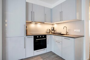 A modern kitchen with white cabinets, a black oven, a coffee maker, and a sink.