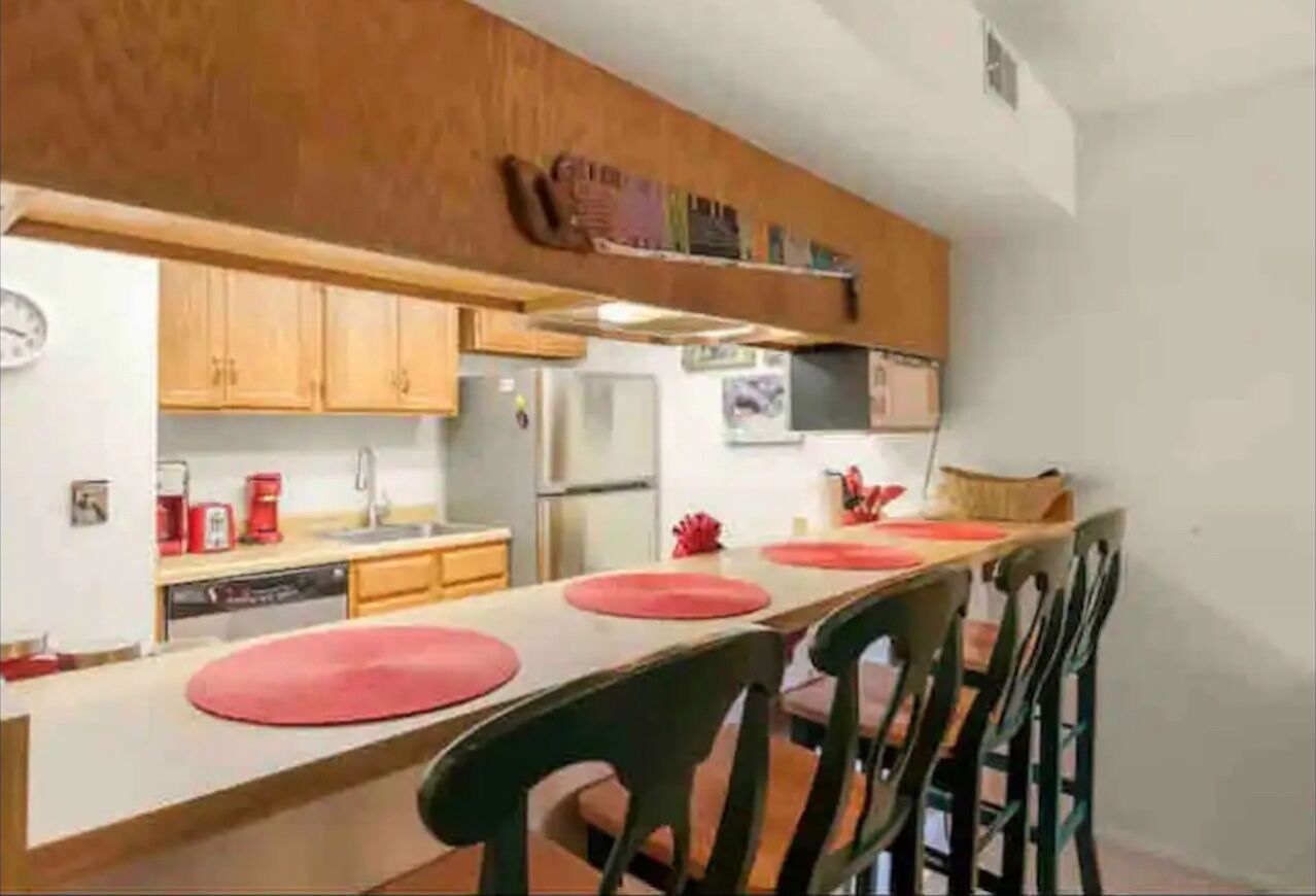 Une cuisine compacte dotée de meubles en bois, d’un réfrigérateur et d’un coin repas avec des chaises et une table.