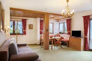 A room with a sofa, dining table, chairs, a television, and a chandelier. - Studio Apartment 'Gästehaus Arkadia - Ferienwohnung 3' with Mountain View, Balcony and Wi-Fi (Garmisch-Partenkirchen)