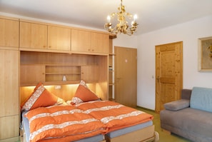 A bedroom with a bed, a sofa, wooden cabinets, a chandelier, and a door. - Studio Apartment 'Gästehaus Arkadia - Ferienwohnung 3' with Mountain View, Balcony and Wi-Fi (Garmisch-Partenkirchen)
