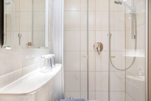 Ein Badezimmer mit Duschkabine aus Glas, einem weißen Waschbecken und einem Spiegel.