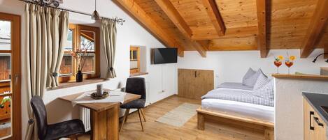 Een knus ingerichte kamer met houten plafond, een bed, bureau met stoel, televisie en raam met gordijnen.