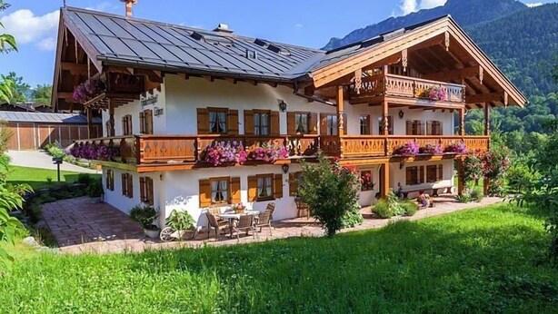 Un chalet à deux étages doté d’un balcon en bois, d’un petit jardin et surplombant un paysage montagneux.