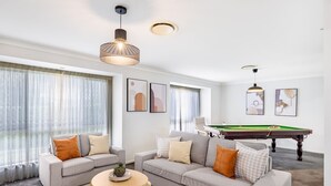 Un salon moderne avec un canapé gris, deux tables d’appoint et une table de billard.