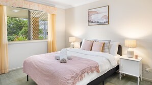 Une chambre à coucher bien rangée, avec un lit, des lampes de chevet, une fenêtre avec des rideaux et un tableau accroché au mur.