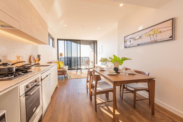 A modern kitchen with a dining area, a view through a glass door, and a dining table set for four.