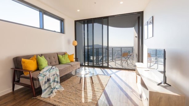 A modern living room with a sofa, coffee table, and a view of the city through large windows. - One bed Apt at Southbank w/ Rooftop Pool&Carpark (South Brisbane)
