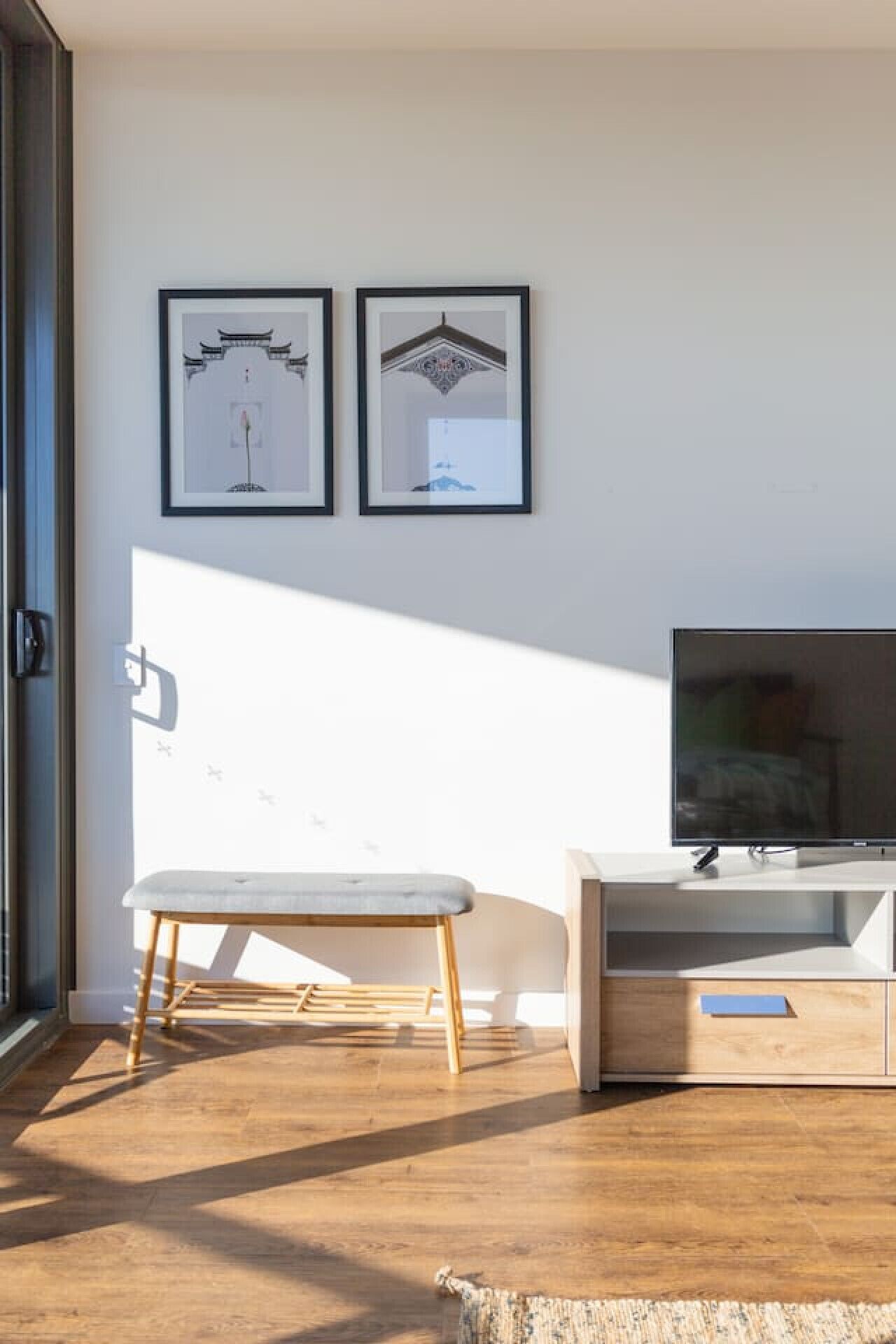 A modern living room with a bench, a TV, and two framed pictures on the wall.