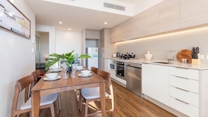 A modern kitchen with white cabinets, a wooden dining table, and a large plant. - One bed Apt at Southbank w/ Rooftop Pool&Carpark (South Brisbane)