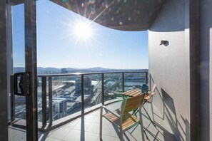 A balcony with a view of a cityscape, a table, and a chair.
