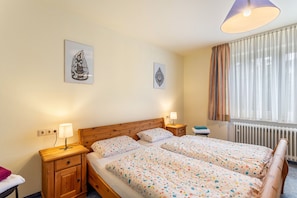 A hotel room with two beds, a wooden headboard, bedside tables with lamps, a window with curtains, and wall art.