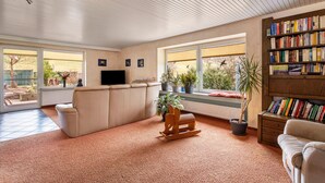 A living room with a sofa, a wooden rocking chair, a bookshelf, and a television. - Holiday Home 'Haus Waldblick' with Private Terrace, Private Garden and Wi-Fi (Bad Berleburg)