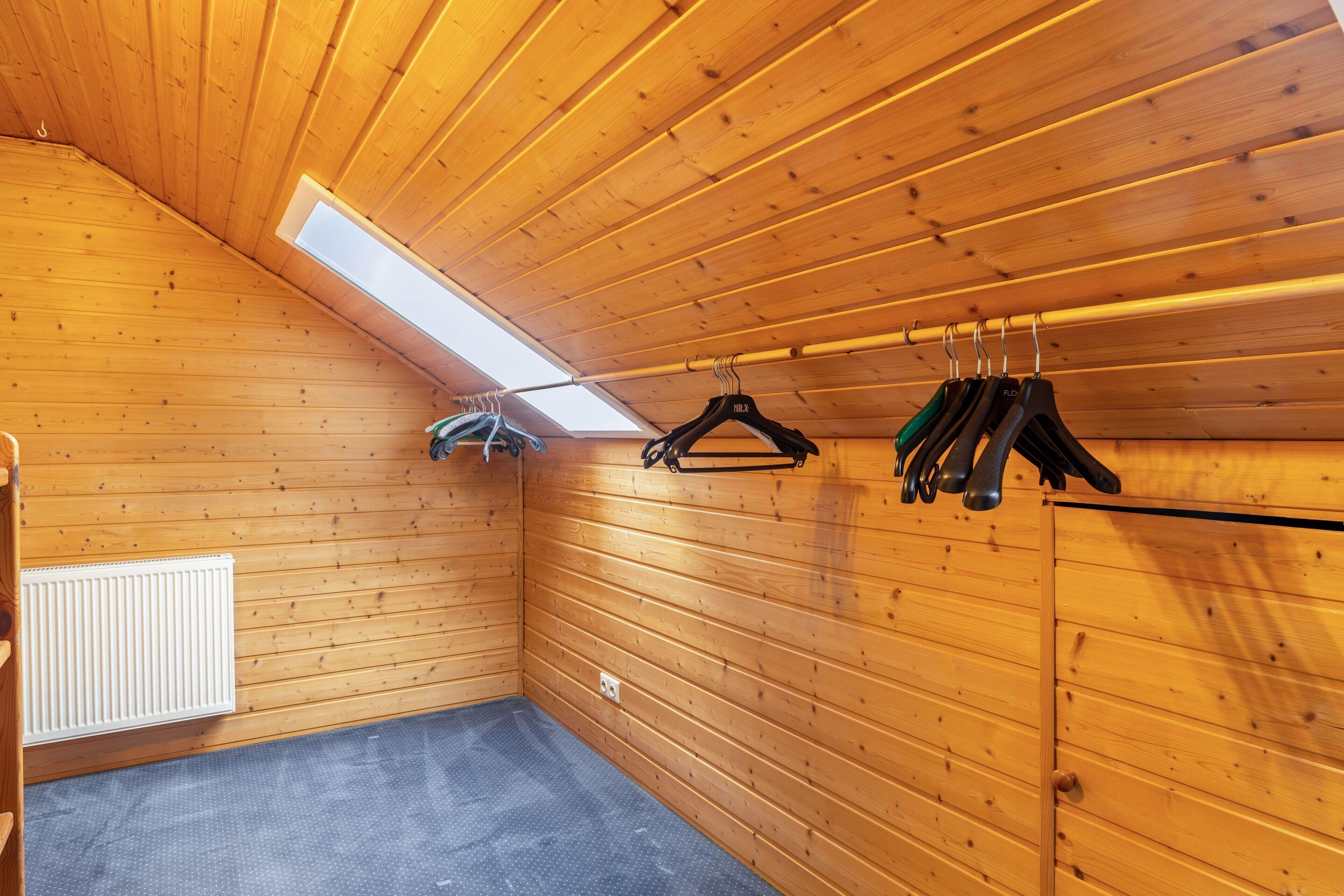 A room with wooden walls, a slanted ceiling, a skylight, a radiator, and a clothes rack with hangers.