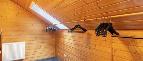A room with wooden walls, a slanted ceiling, a skylight, a radiator, and a clothes rack with hangers.