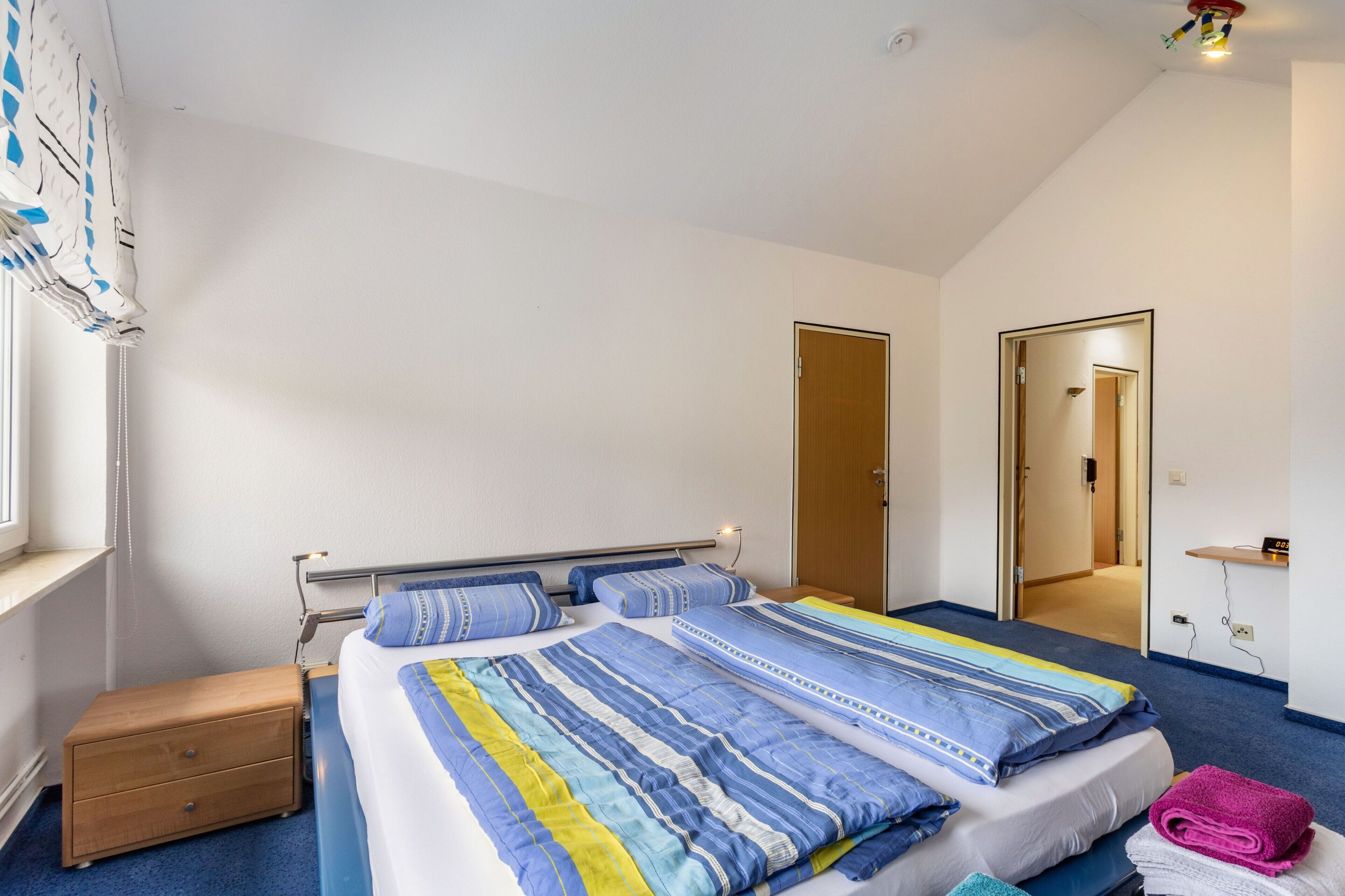 A bedroom with a bed, a nightstand, a window, and a door.
