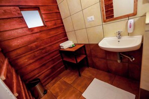 Un bagno compatto con pareti in legno, un piccolo oblò, un lavandino e uno specchio.