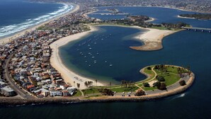 Vue aérienne d’une ville côtière, avec un port de plaisance, des plages de sable et une zone densément peuplée, caractérisée par de nombreux immeubles.