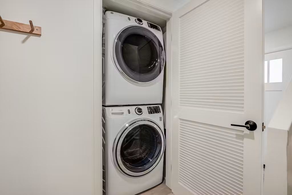 Un cuarto de lavandería con dos lavadoras apiladas de carga frontal y una puerta cerrada con picaporte.