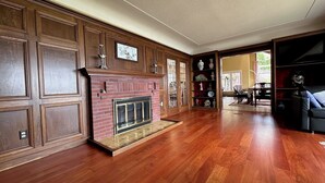 Un vaste salon doté d’un parquet en bois, d’une cheminée en briques et d’un grand mur recouvert de panneaux de bois.
